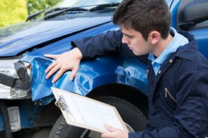 Auto Workshop Mechanic Inspecting Damage To Car